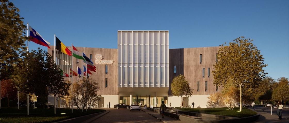 Front view of the European Centre for Medium-Range Weather Forecasts (ECMWF) Headquarters, showing a modern facade with tall glass panels and a row of international flags at the entrance.