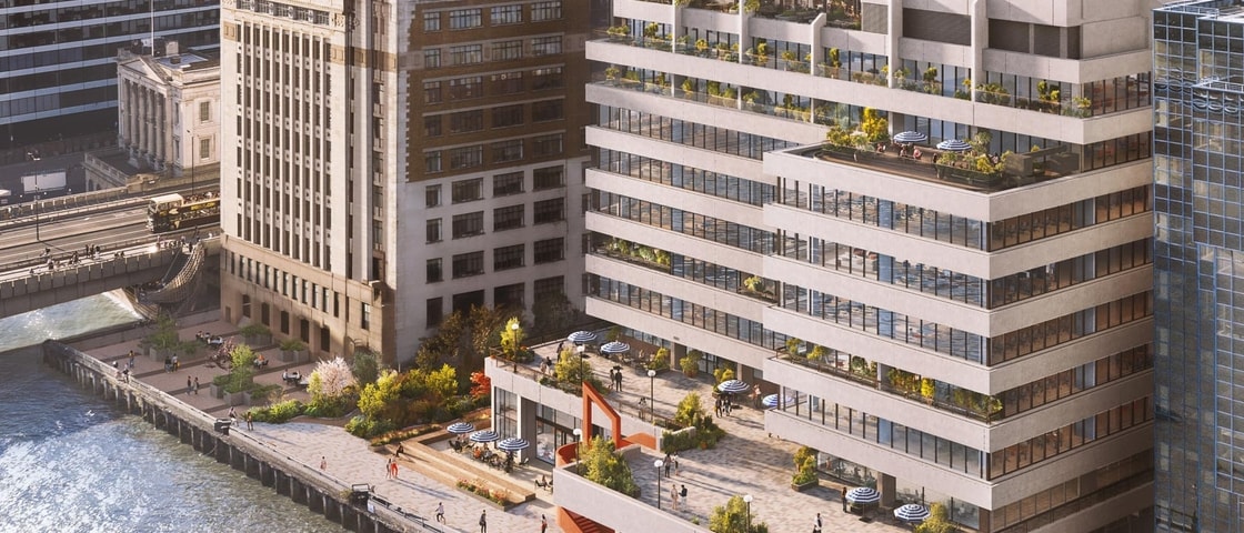 A CGI aerial rendering of a contemporary riverside office development alongside the River Thames in London. The stepped building features extensive floor-to-ceiling glazing, landscaped terraces, rooftop gardens and outdoor seating areas. A large waterfront plaza with planting, trees and public seating overlooks a pedestrian promenade running along the river’s edge. Several people are visible throughout the public spaces, while neighbouring city buildings and a bridge span the water in the background.
