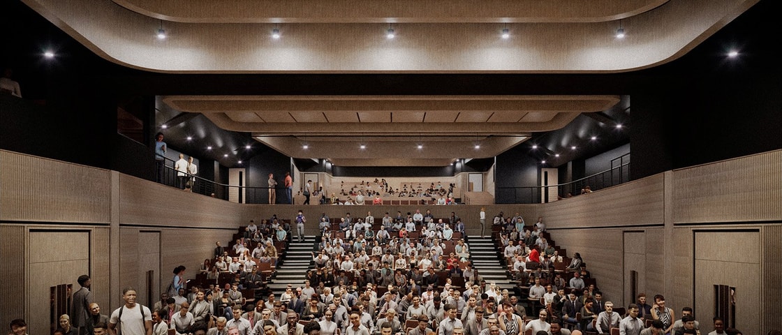 A CGI of a large modern auditorium filled with seated attendees facing the stage, with additional people visible on the upper balcony level.