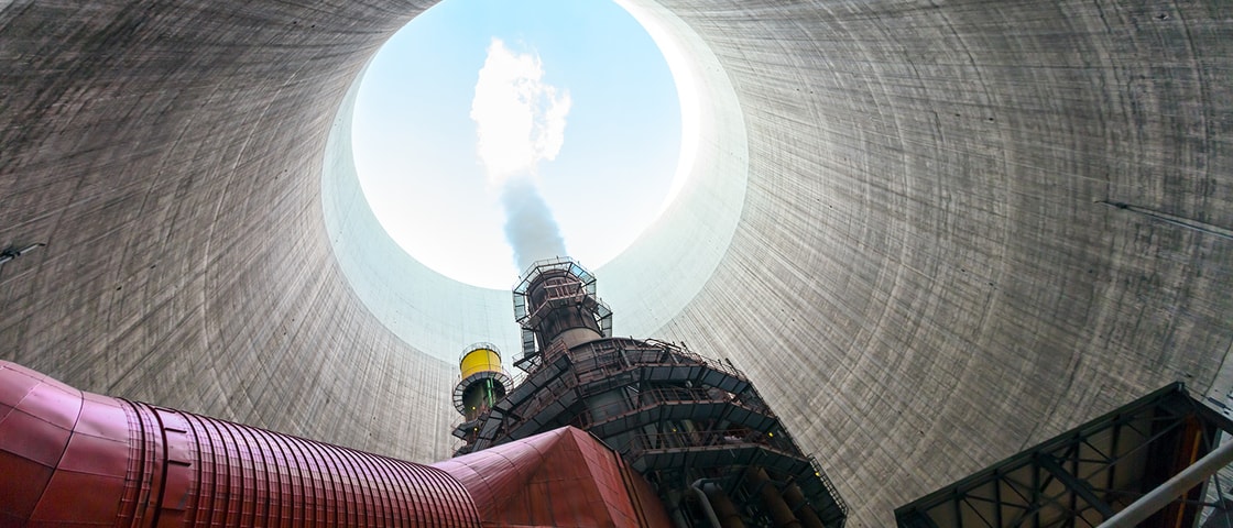Upward view from inside a large industrial cooling tower, showing red and steel infrastructure rising toward a circular opening where steam vents into the sky above.