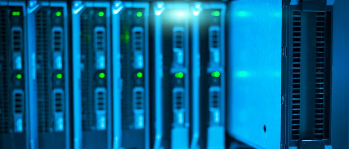 Close‑up of server racks in a data centre, showing illuminated status lights and cooling vents in a blue‑lit technical environment.