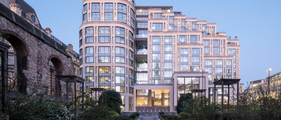 Modern building with glass windows and balconies next to an old stone structure.