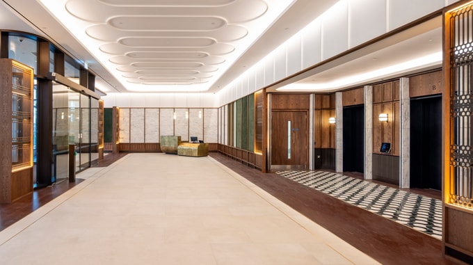 Modern office reception with a sculpted illuminated ceiling, timber and marble finishes, a reception desk and lift lobby areas.