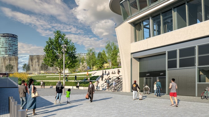 View of the HS2 Curzon Street station entrance area, showing a modern building façade with large windows and lift access, and a landscaped public space with tiered seating, trees, and pathways where people are walking and gathering.