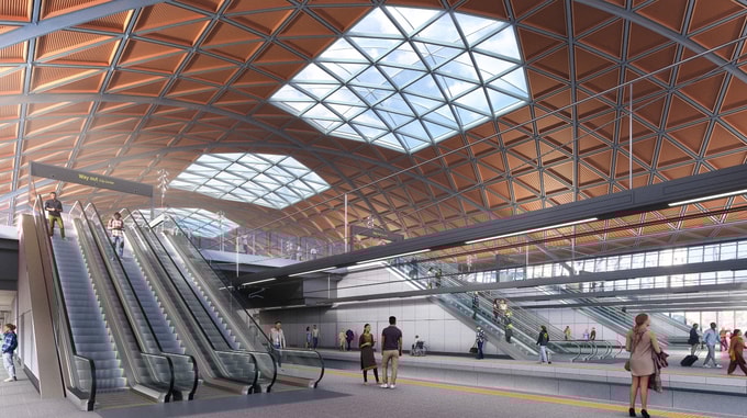 Interior view of the HS2 Curzon Street station concourse, showing wide escalators leading to upper levels beneath a large timber-lined roof with geometric skylights, and people moving through the spacious platform area.