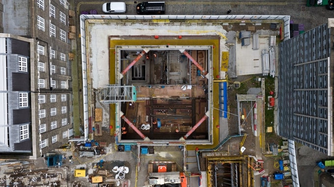 Aerial view of the HS2 Euston construction site showing a rectangular excavation with steel framework, scaffolding and construction equipment, surrounded by city buildings.
