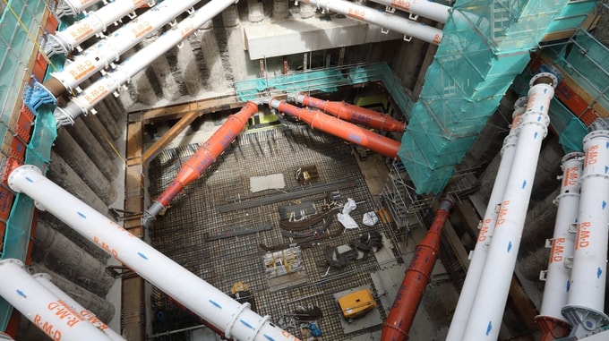 Top‑down view of underground construction works at HS2 Euston, showing large temporary support pipes, reinforced concrete works, scaffolding, and construction equipment within a deep excavation.