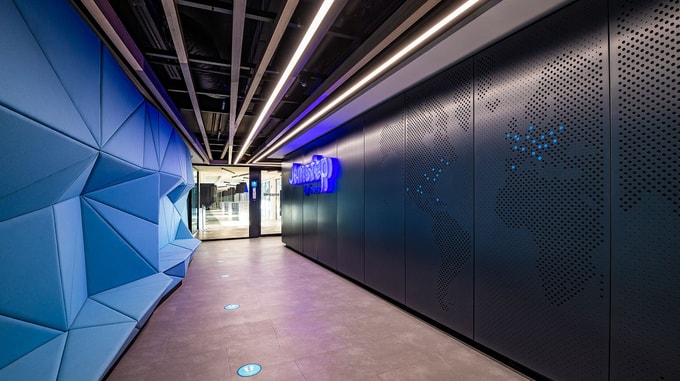 A stylish hallway with geometric blue panels, perforated black walls displaying dotted world maps, and a glowing "Jemstep" sign.