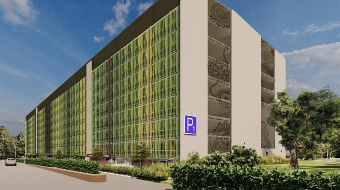 A modern parking structure with green patterned glass and a large "P1" sign, surrounded by trees and landscaped greenery.
