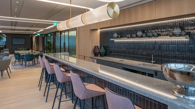 Interior view of the Taylor Wessing office featuring a modern bar area with minimalist design, warm wood finishes, and ambient lighting.