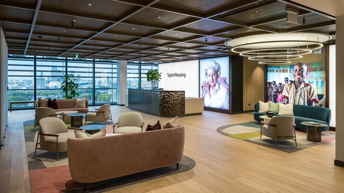 Curved seating area at Taylor Wessing featuring soft grey upholstery, circular lighting fixtures, and a sculptural ceiling design that adds depth to the modern lounge space.