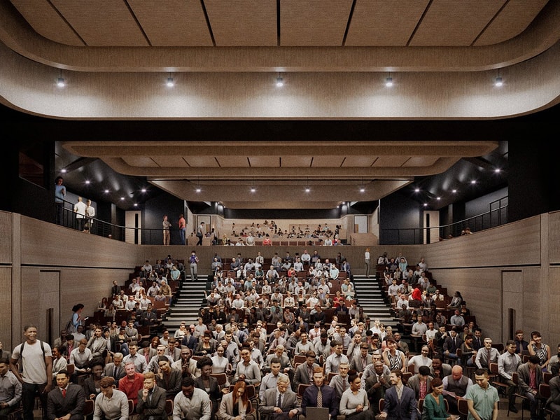 A CGI of a large modern auditorium filled with seated attendees facing the stage, with additional people visible on the upper balcony level.