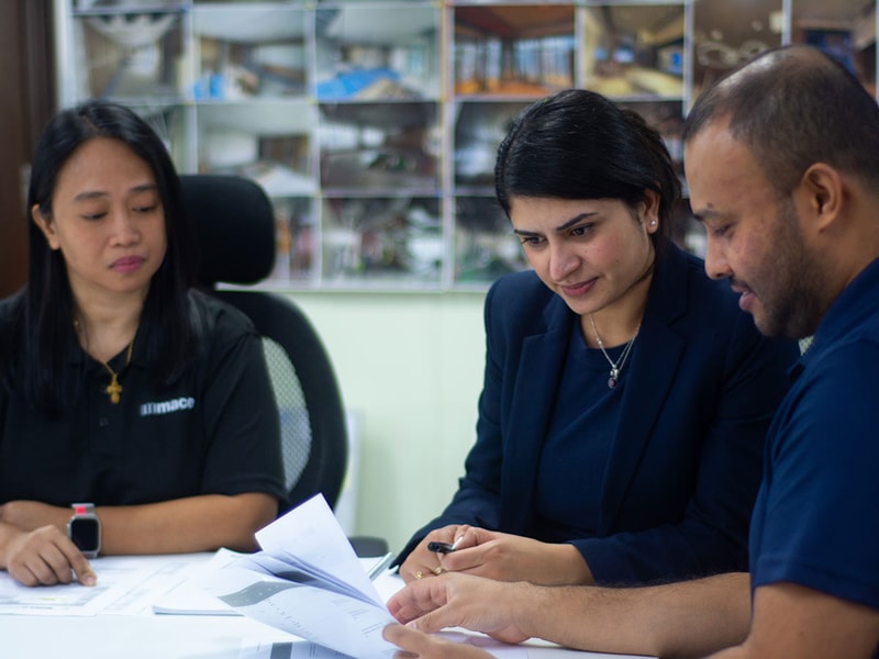Three people are looking through documents while sat around a meeting room table