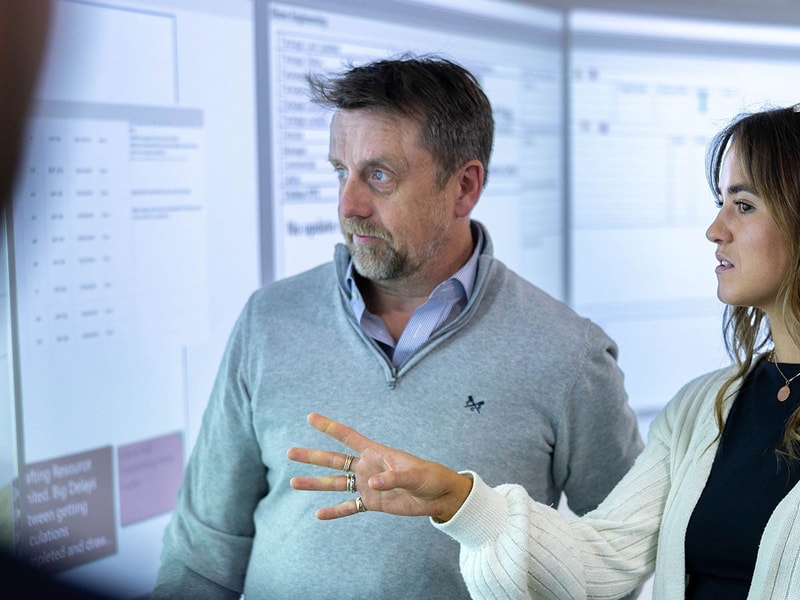 man and women are discussing data presented on a 180 degree command room projector wall
