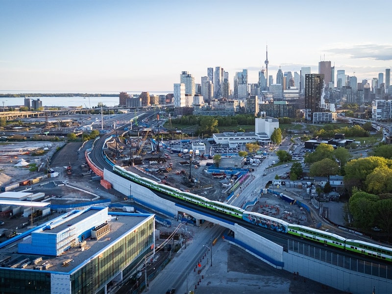 Aerial view of a cityscape featuring a train traveling along the tracks amidst buildings and streets below.