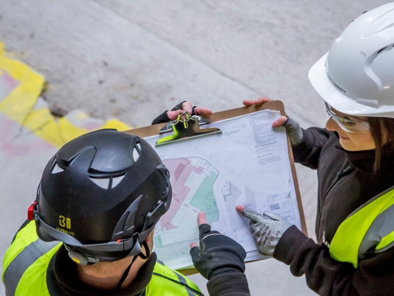 Two colleagues wearing hi-vis jackets and hard hats reviewing a piece of printed documentation