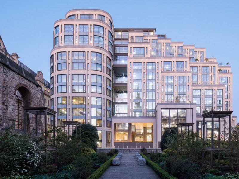 Modern building with glass windows and balconies next to an old stone structure.